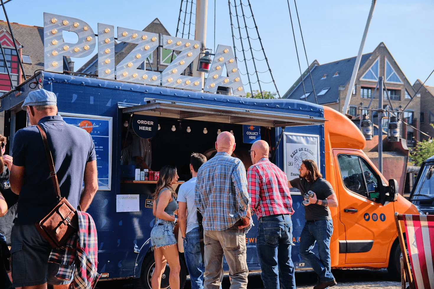 Photo of people lining up and standing around a van which has the words PIZZA at the top